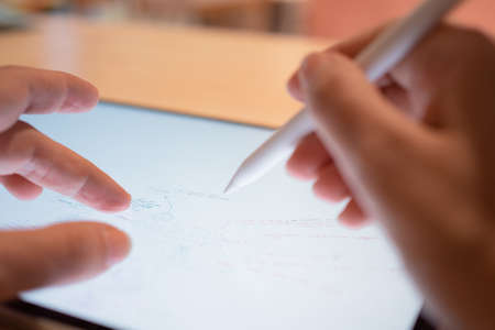 Plan and make notes by hand on a digital tablet, lists and flowcharts in the editor. The hand draws on the tablet screen using a stylus. close-up small depth of fieldの写真素材