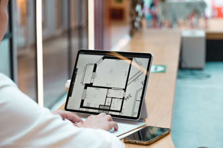 An architect engineer works remotely, freelance work on a laptop, concept. A device with a floor plan on the screen, hands on the keyboard, close-upの写真素材