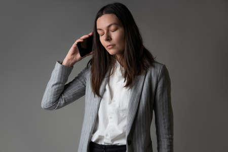 businesswoman dressed in a jacket and trousers in a casual style uses a smartphone for work and...
