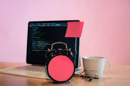 Its time to learn programming languages, call to action, concept. Training in programming and improving skills in code and application development. Laptop and alarm clock with closed dial on a pinkの写真素材