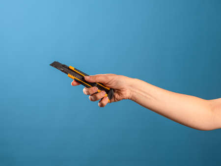 Cut or shorten something, cut it out. A female hand holds a stationery knife with a retractable blade, blue backgroundの写真素材