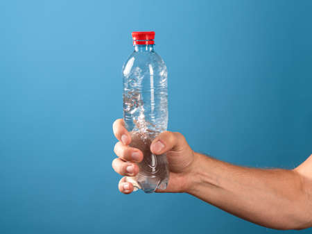 Drink water. The benefits of drinking clean water for the health of the body and well-being. A mans hand hands you a bottle of liquid. Blue background.の写真素材