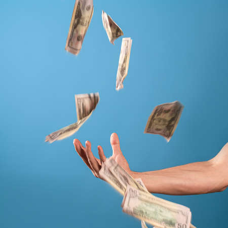 Earn money, get a good revenue. A mans hand and a lot of cash, a photo on a blue backgroundの写真素材