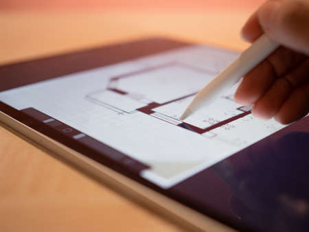 architectural engineer is working on a floor plan of building on mobile tablet computer. architects...