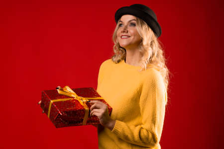 Winter holiday, a young woman in knitted clothes and a bowler hat, holding a gift box with a ribbon