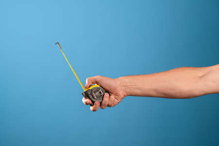 Measure it, a yellow construction tape measure to measure the length of something. Roulette with a measured segment in a mans hand, blue backgroundの写真素材