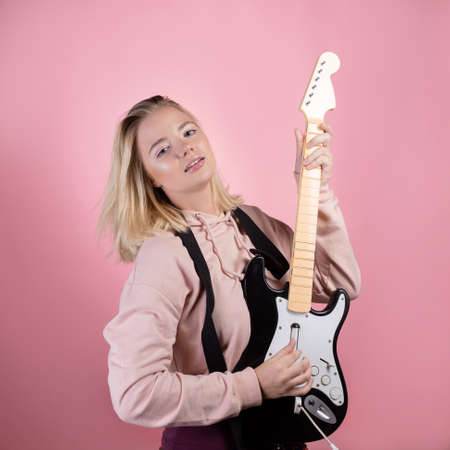 Play the guitar, pretend that you are a guitarist, a game guitar. Young woman on a pink background