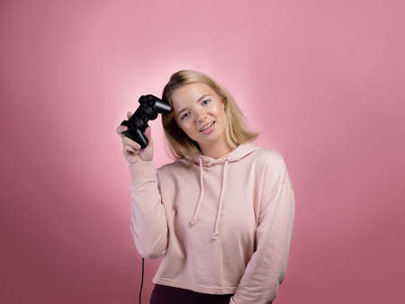 A gamer who is passionate about the process. A cute blonde is holding a gamepad in her hands,...