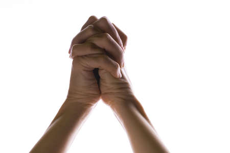 Praying crossed hands on a white background. Light from above. Hands folded in prayer. Hand gestures