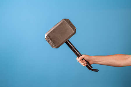Be a hero, perform a feat. The Scandinavian hammer , Mjolnir in a mans hand. Photo on a blue backgroundの写真素材