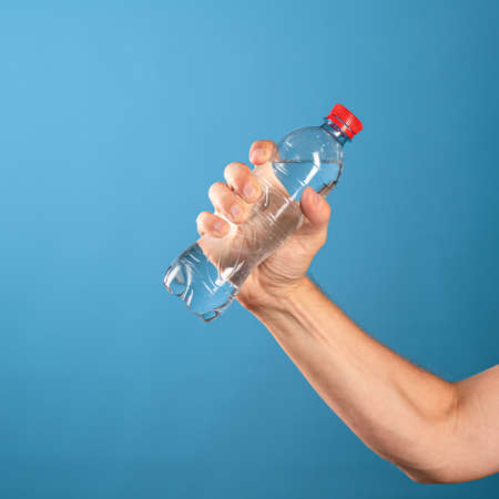 Drink water. A mans hand gives a bottle of clean drinking water. Close-up on a blue background