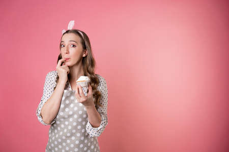 young charming female pastry chef tastes a muffin with cream. A cook in a polka-dot apron. pastry...