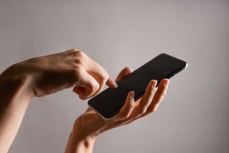 Use mobile apps, scroll. Smartphone, the female hand uses the touchpad, Layout for design, mockup. contrast light. light grey backgroundの写真素材