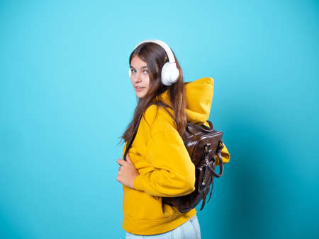 A young smiling student with a backpack and headphones, listening to music or recording a lecture. A young brunette in a bright yellow hoodie uses a mobile app to listen to audioの写真素材