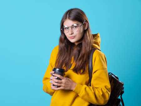 Cute young brunette in jeans and yellow hoodie. A beautiful student in glasses with a backpack on...