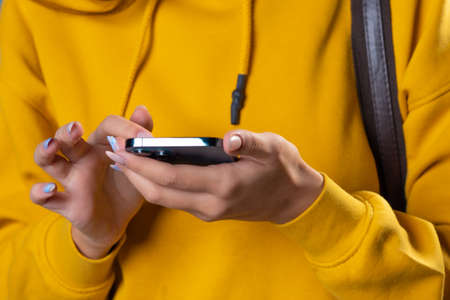 Mobile communication, use social network applications and instant messengers for correspondence. young brunette in yellow uses smartphone to communicate and search information on Internet, close-upの写真素材