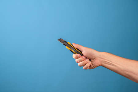 Cut or shorten something, cut it out. A mans hand holds a stationery knife with a retractable blade, blue backgroundの写真素材