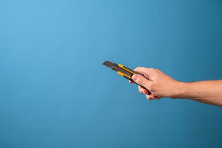 Cut or shorten something, cut it out. A mans hand holds a stationery knife with a retractable blade, blue backgroundの写真素材