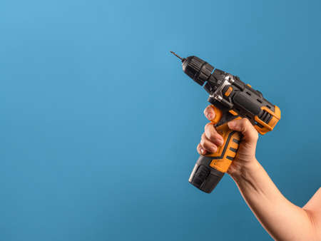 Fix it, fix a malfunction or tighten a bolt on a construction site. A female hand holds a screwdriver or drill, a repair tool, a photo on a blue background.の写真素材