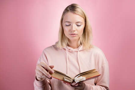 Fascinating reading, serious study of educational materials, an open book with a large number of bookmarks in the hands of a student. A young woman in a pink hoodie with a textbook in her hands,の写真素材