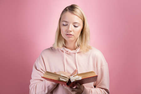 Fascinating reading, serious study of educational materials, an open book with a large number of bookmarks in the hands of a student. A young woman in a pink hoodie with a textbook in her hands,の写真素材