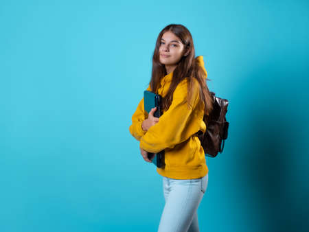 Internet work and e-education, a student or a freelancer works remotely. A student with a laptop in her hands, a young brunette in a yellow hoodie on a blue backgroundの写真素材