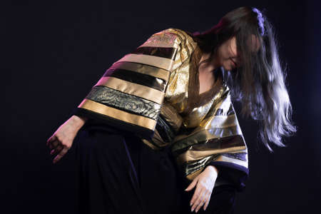 Stylish and daring image, futuristic fashion. A young woman in a multicultural outfit mixing Asian and European style, a golden kimono shirt and trousers, photo in the studio on blackの写真素材