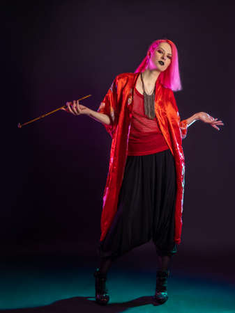 Futuristic look, multicultural outfit, young woman with pink hair in modern trousers, vintage kimono and smoking a pipe in her handsの写真素材