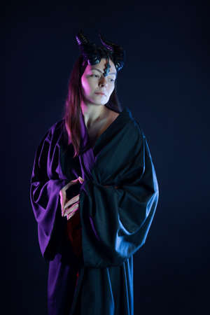 A demoness with horns and in a black kimono with a red belt, a costume of a mystical creature, a young woman in a fantasy gothic image, a portrait on blackの写真素材