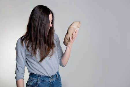 A young woman hides her face behind a mask, the concept of psychological problems, a crisis of self-identification or strong shyness. Photos in light gray tones, gray background.の写真素材