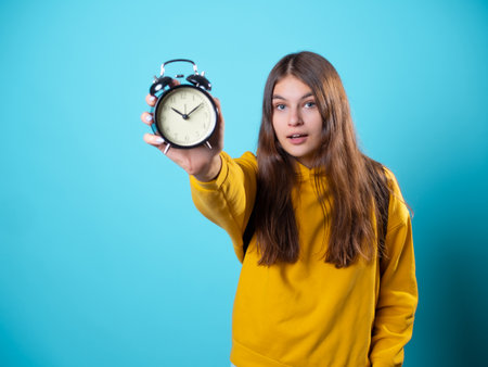 Hurry up, concept. A young brunette in a youth hoodie holds an alarm clock in her hands and hurriesの写真素材