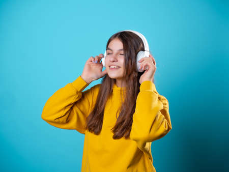 A young smiling student wearing headphones, listening to music. A young brunette in a bright yellow hoodie uses a mobile app to listen to audioの写真素材