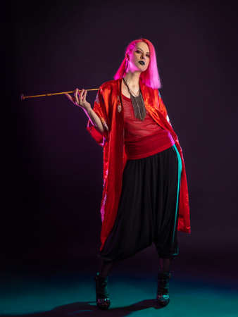 Futuristic look, multicultural outfit, young woman with pink hair in modern trousers, vintage kimono and smoking a pipe in her handsの写真素材