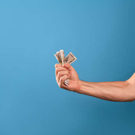 Earn money, get a good revenue. A mans hand and a lot of cash, a photo on a blue backgroundの写真素材