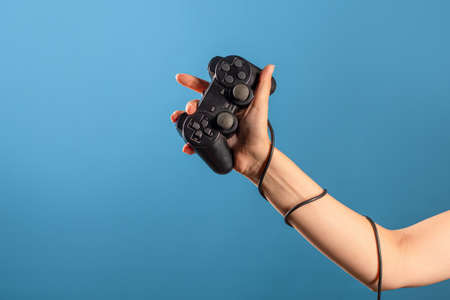 Play computer games, a hobby is computer video games, a joystick in your hand. A female hand holds a gamepad with a wire, a photo on a blue backgroundの写真素材