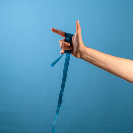 Lose weight, get rid of excess weight, a call to engage in health. A female hand holds a centimeter ribbon in his fist, blue backgroundの写真素材