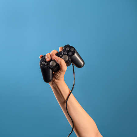 Play computer games ,become a professional gamer. A female hand holds a gamepad with a wire, a photo on a blue backgroundの写真素材