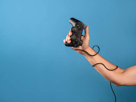 Play computer games, a hobby is computer video games, a joystick in your hand. A mans hand holds a gamepad with a wire, a photo on a blue backgroundの写真素材