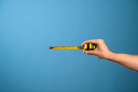 Measure it, a yellow construction tape measure to measure the length of something. Roulette with a measured segment in a mans hand, blue backgroundの写真素材