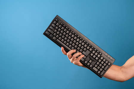 Program, learn programming and computer science, write code. A man holds a computer keyboard in his hands, a blue background.の写真素材