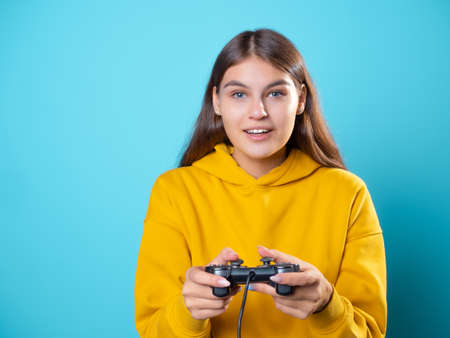 A gamer girl, a young brunette in a yellow hoodie, clutches a gamepad in her hands and looks at the monitor , an exciting gameplayの写真素材