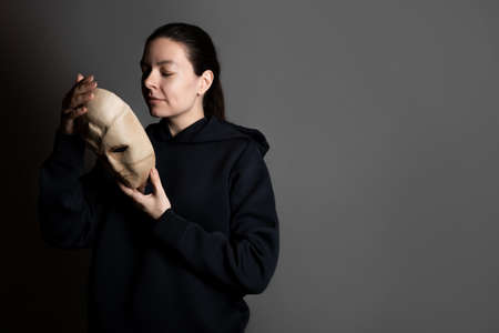 Remove the mask, reveal the identity, express yourself in something, the concept. A young woman in a black hoodie holds a mask in her hands, removing it from her face.の写真素材