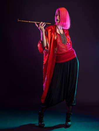 Futuristic look, multicultural outfit, young woman with pink hair in modern trousers, vintage kimono and smoking a pipe in her handsの写真素材