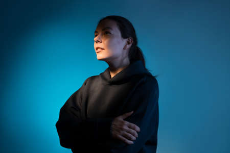 Think, there is an idea. Young woman portrait side view, face partially illuminated, thoughtful look up, dark blue backgroundの写真素材