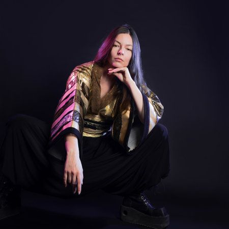 Stylish and daring image, futuristic fashion. A young woman in a multicultural outfit mixing Asian and European style, a golden kimono shirt and trousers, photo in the studio on blackの写真素材