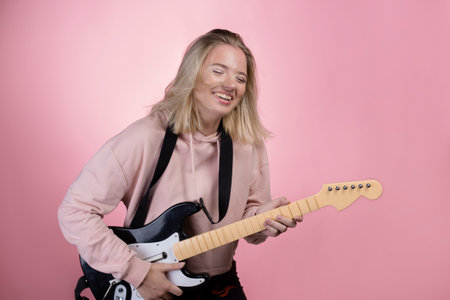 Play the guitar, pretend that you are a guitarist, a game guitar. Young woman on a pink backgroundの写真素材