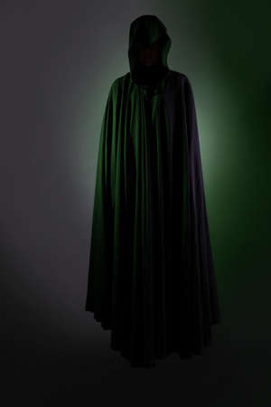 A flying mystical vampire in a black hoodie, a figure hovering in the air, a face hidden by a hood, a dark background green backlightの写真素材