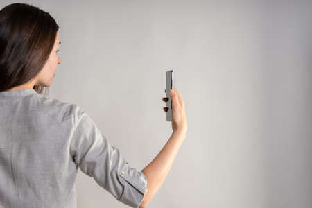 woman holds a smartphone in front of her eyes, use the app or take a photo. layout for your design. Hand gestures, light grey backgroundの写真素材