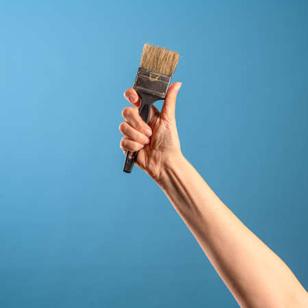 Update the interior, paint the walls, decor in the house. A female hand stretches out a paint brush, blue backgroundの写真素材