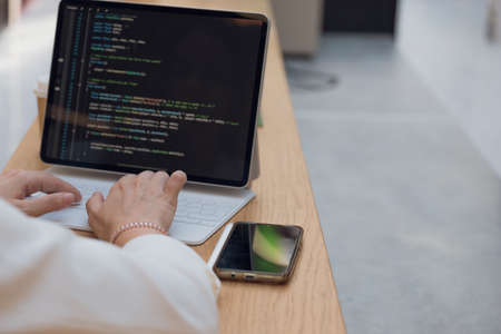 A freelance programmer works remotely, a young woman sits at a table in a coworking or business center and works at a laptop, computer screen and hands on the keyboard close-upの写真素材